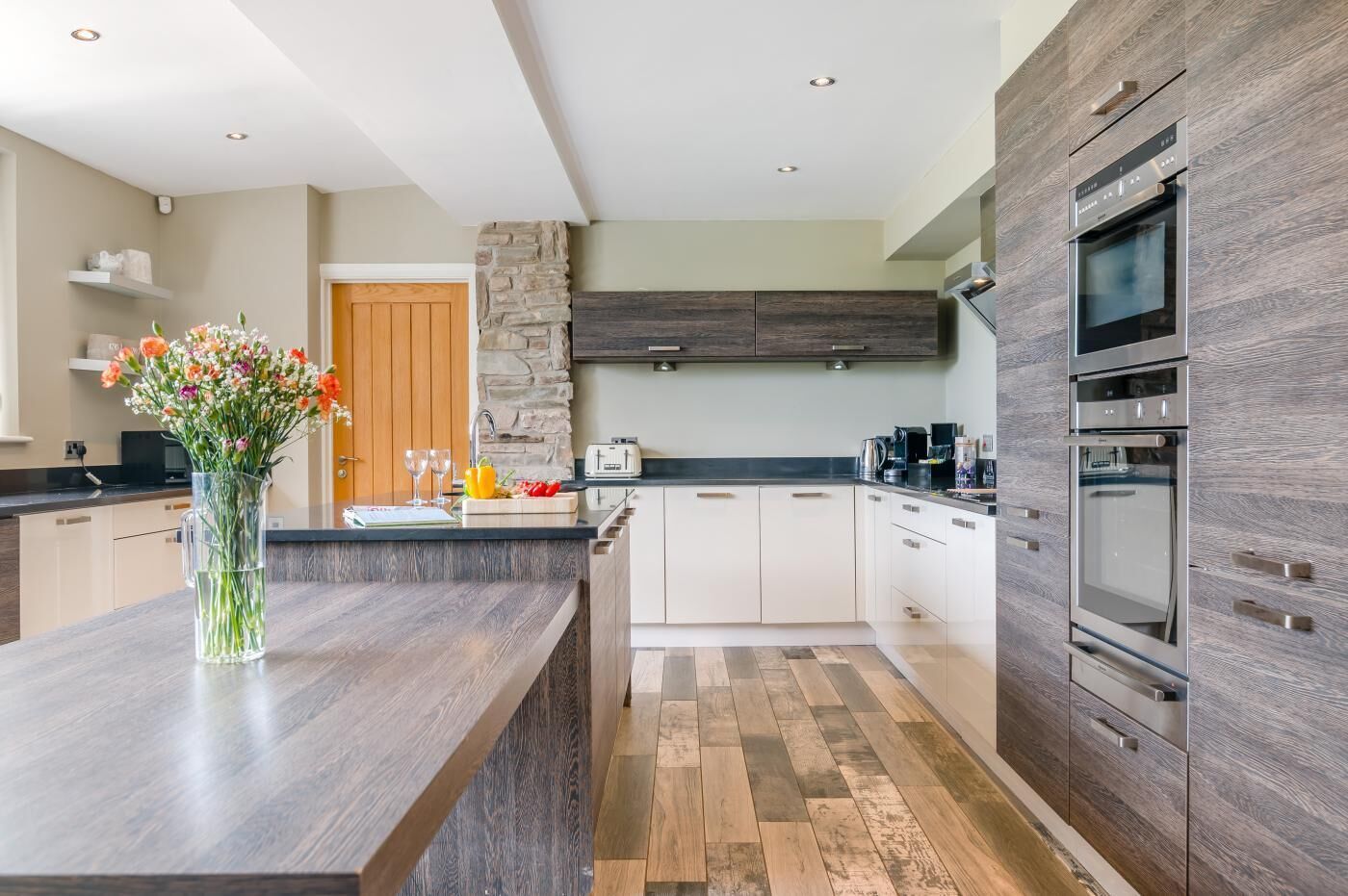 A modern kitchen with a central island, a stone accent wall, and built-in appliances.