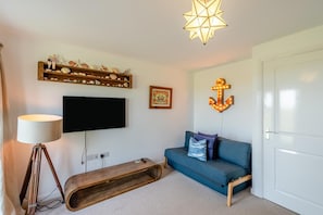 A room with a flat-screen TV, a wooden bench, a blue sofa, a starfish shelf, and a lit anchor decoration.