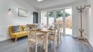 Un comedor con una mesa de madera dispuesta para cuatro personas, un sofá amarillo y una lámpara de pie.