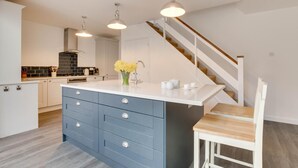 Una cocina moderna con una isla central, armarios blancos y una escalera de madera.