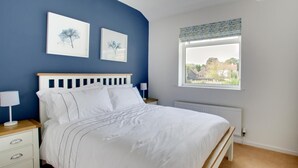 Un dormitorio con cama, mesitas de noche, una ventana con vistas y una obra de arte en la pared.