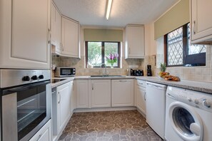 A compact kitchen with white cabinets, a built-in oven, a microwave, a sink, and a washing machine. - 3 Bed in Ravenscar (oc-sa397) (Ravenscar)