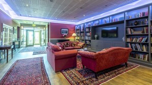 A spacious living room with a red sofa set, a coffee table, and a bookshelf filled with books. - 7 Bed in Northrepps (oc-n32549) (Overstrand)