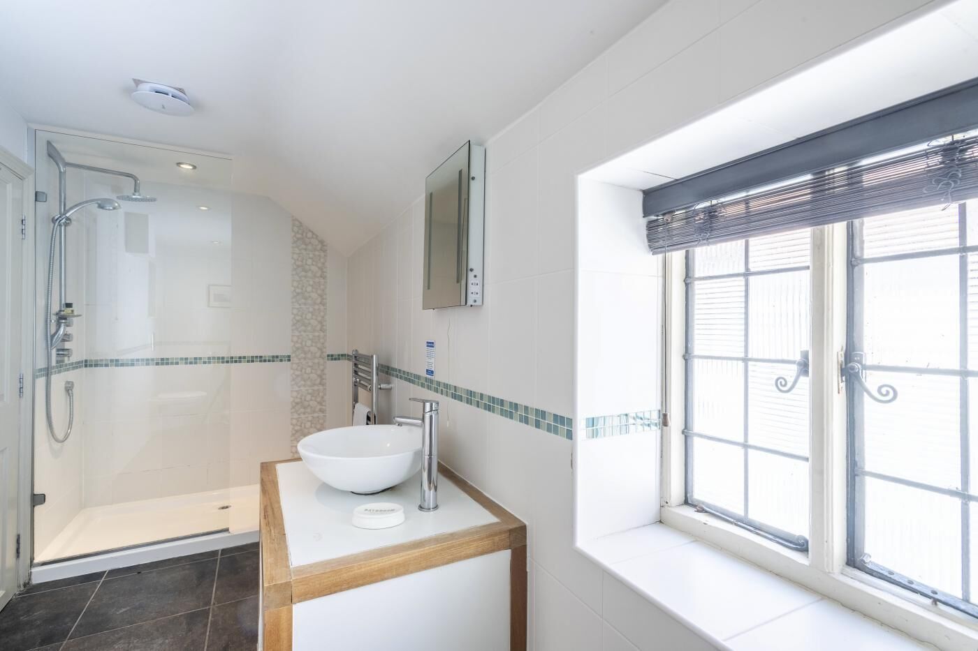 A modern bathroom with a glass-enclosed shower, a white sink, and a window with a metal grill.