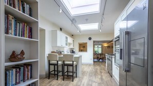 A modern kitchen with a built-in refrigerator, a dining area with two chairs, and a bookshelf filled with books. - 7 Bed in Northrepps (oc-n32549) (Overstrand)