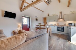 A cozy living room with a sofa, a TV, and a dining area with chairs and a table. The kitchen has white cabinets, a microwave, and a stove. - 2 Bed in Saltburn-by-the-sea (oc-wa021) (Easington)