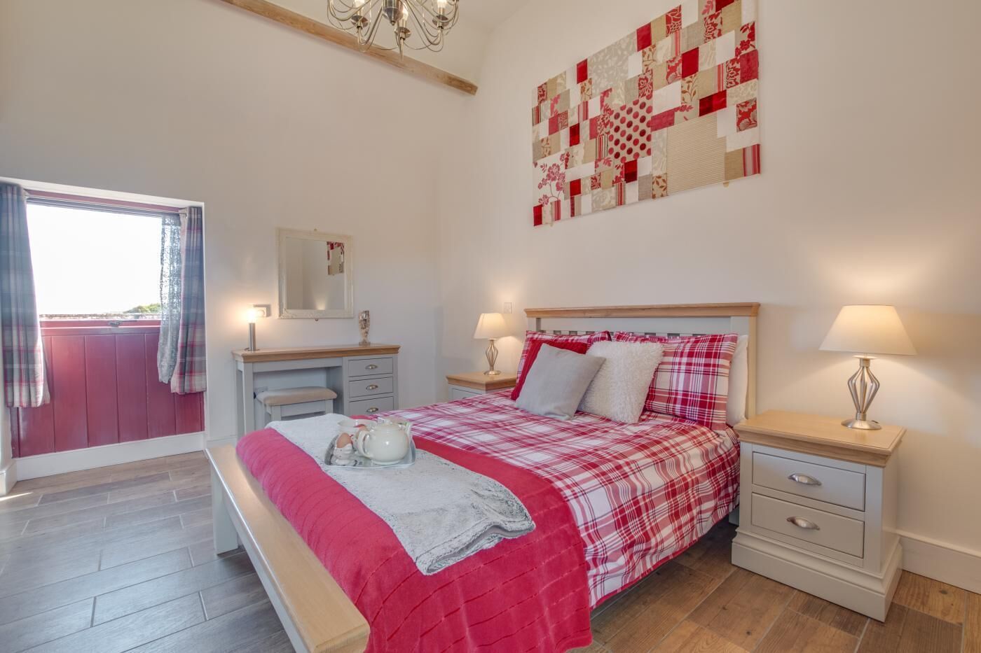 A bedroom with a bed, bedside tables, a dresser, a mirror, and a quilt on the wall.