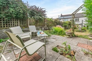 A patio with outdoor seating, a table with a newspaper, and a garden with flowers and plants. - 2 Bed in Higher Penponds (oc-h32383) (Camborne)