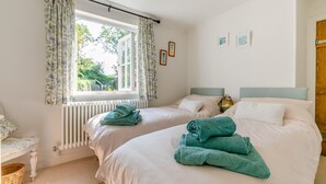 Een slaapkamer met twee bedden, een raam met gordijnen, een radiator en een lamp.