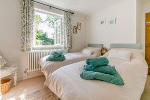 Une chambre avec deux lits, une fenêtre avec des rideaux, un radiateur et une lampe.