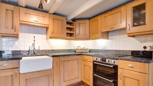 A kitchen with wooden cabinets, a granite countertop, a stainless steel sink, a built-in oven, and a clock. - 2 Bed in Whitby (oc-r579) (Robin Hood's Bay)
