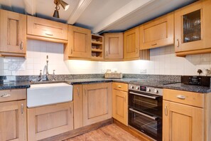 A kitchen with wooden cabinets, a granite countertop, a stainless steel sink, a built-in oven, and a clock. - 2 Bed in Whitby (oc-r579) (Robin Hood's Bay)