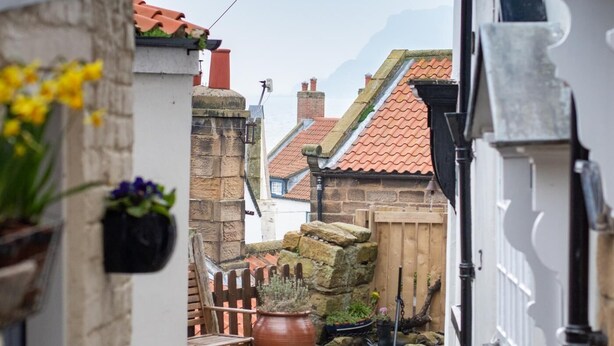 A narrow alleyway with stone paving, a wooden bench, and potted plants. - 2 Bed in Whitby (oc-r579) (Robin Hood's Bay)