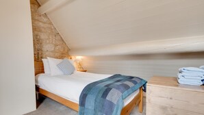A bedroom with a bed, a nightstand, a lamp, a wooden dresser, and a stone wall. - 2 Bed in Whitby (oc-r579) (Robin Hood's Bay)