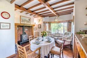 A dining area with a round table set for four, surrounded by wooden chairs. A brick fireplace is visible in the background, and the room features exposed wooden beams on the ceiling. - 3 Bed in Goathland (oc-c32364) (Woodlands)