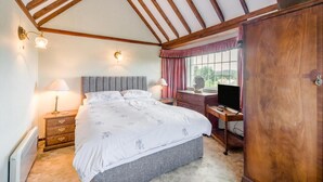 Een slaapkamer met een bed, nachtkastjes, een kaptafel, een televisie en een raam met gordijnen.