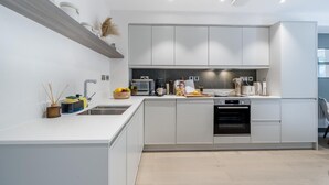 Una cocina moderna con armarios blancos, horno integrado y pileta de acero inoxidable.