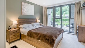 Un dormitorio moderno con una cama grande, mesitas de noche y vistas a un jardín a través de una puerta corrediza de vidrio.