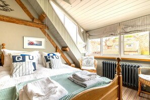 A bedroom with a bed, pillows, a chair, a window with a view, and a radiator. - 2 Bed in Whitby (oc-r038) (Robin Hood's Bay)