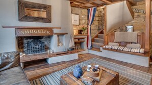Ein gemütliches Wohnzimmer mit Kamin, Holzbalken, einer Steinwand, einer Treppe und einer Bank mit Kissen.