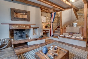A cozy living room with a fireplace, wooden beams, a stone wall, a staircase, and a bench with cushions. - 2 Bed in Whitby (oc-r038) (Robin Hood's Bay)