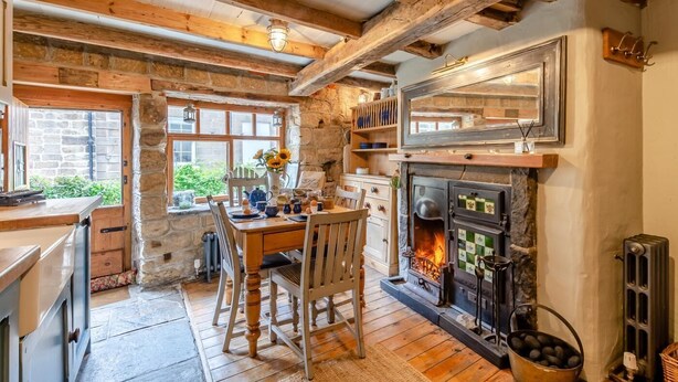 Eine rustikale Küche mit Steinwand, Holzbalken, Kamin und Essbereich mit Tisch und Stühlen.