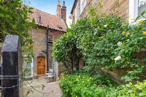 A stone building with a tiled roof, a wooden door, and a small outdoor seating area with a table and chairs. - 2 Bed in Whitby (oc-r038) (Robin Hood's Bay)
