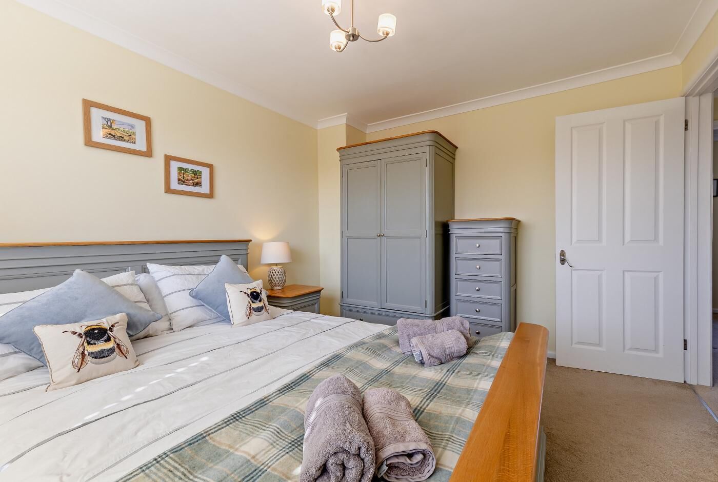 Un lit bien fait, avec des oreillers et une couverture, une table de chevet avec une lampe, une armoire et une porte dans une pièce aux murs de couleur crème.
