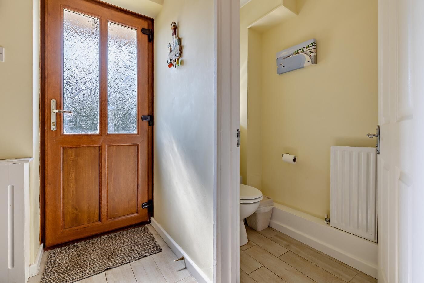 A wooden door with frosted glass panels, a white radiator, a toilet, and a small shelf with items on the wall.