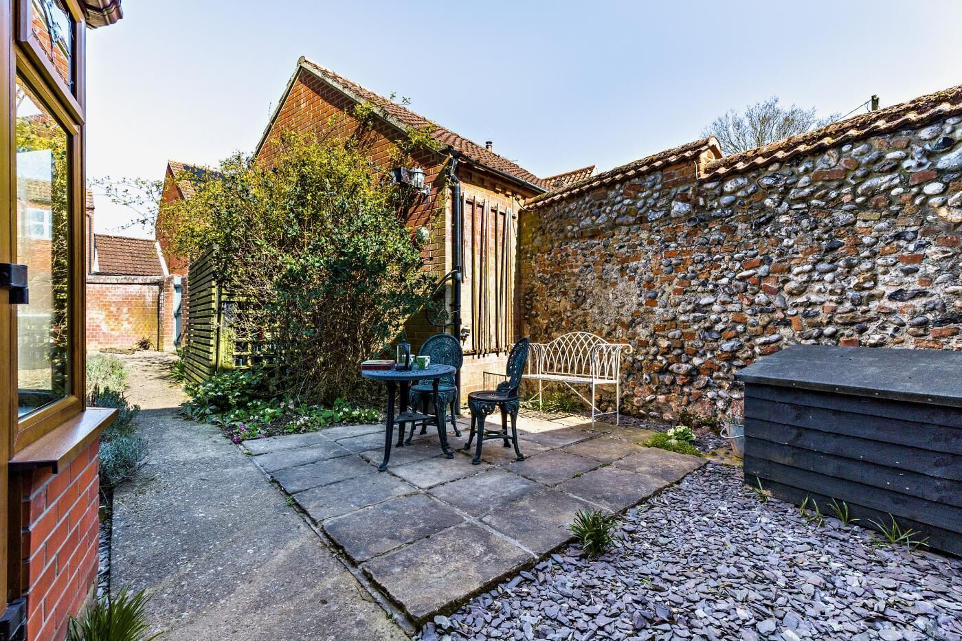A patio with a stone wall, a wooden bench, and a table with chairs.