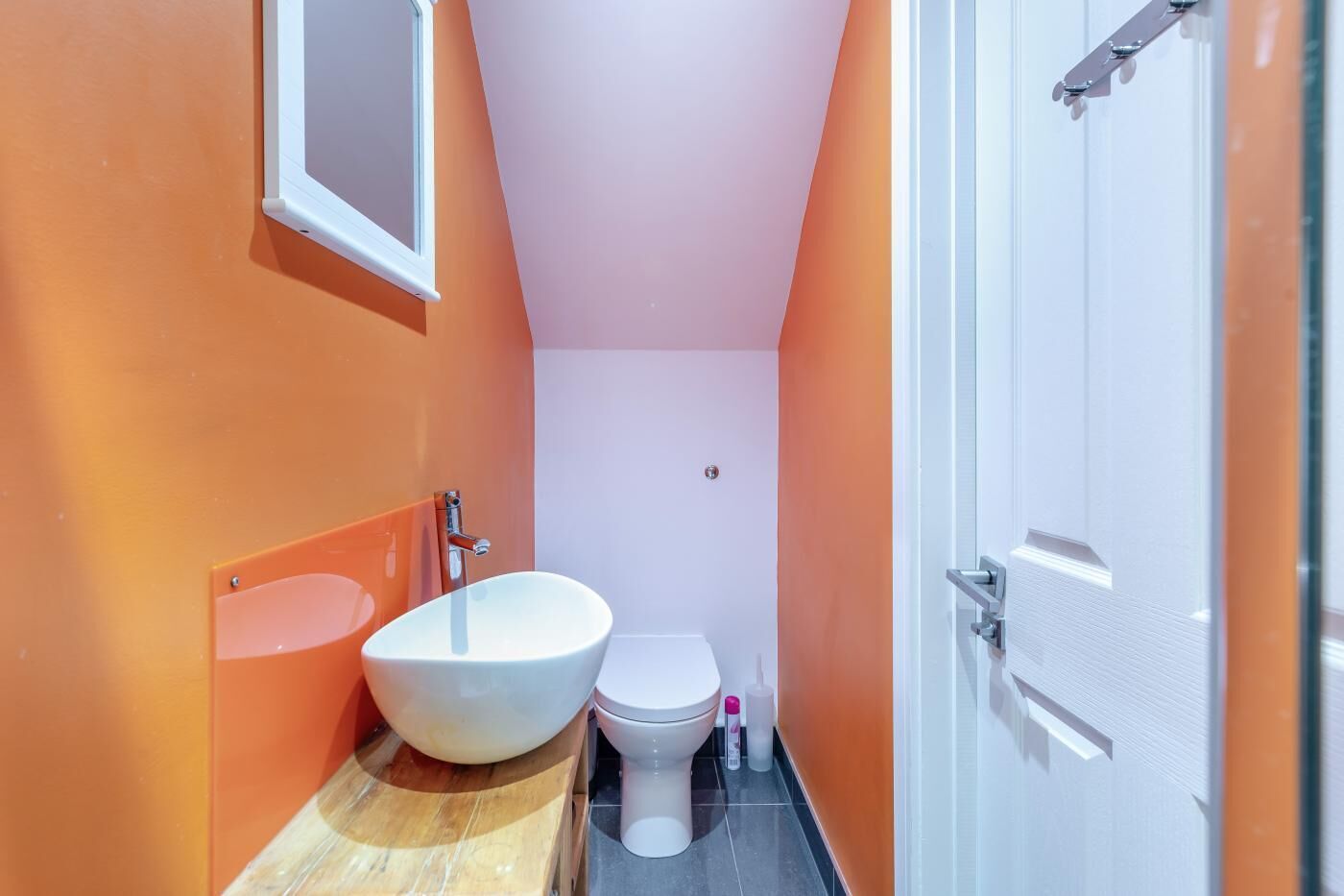 A narrow bathroom with orange walls, a white sink, and a white toilet.