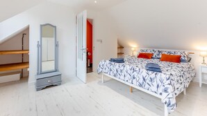 Ein Schlafzimmer mit Bett, Schminktisch, Spiegel und einer Tür zu einem weiteren Raum.