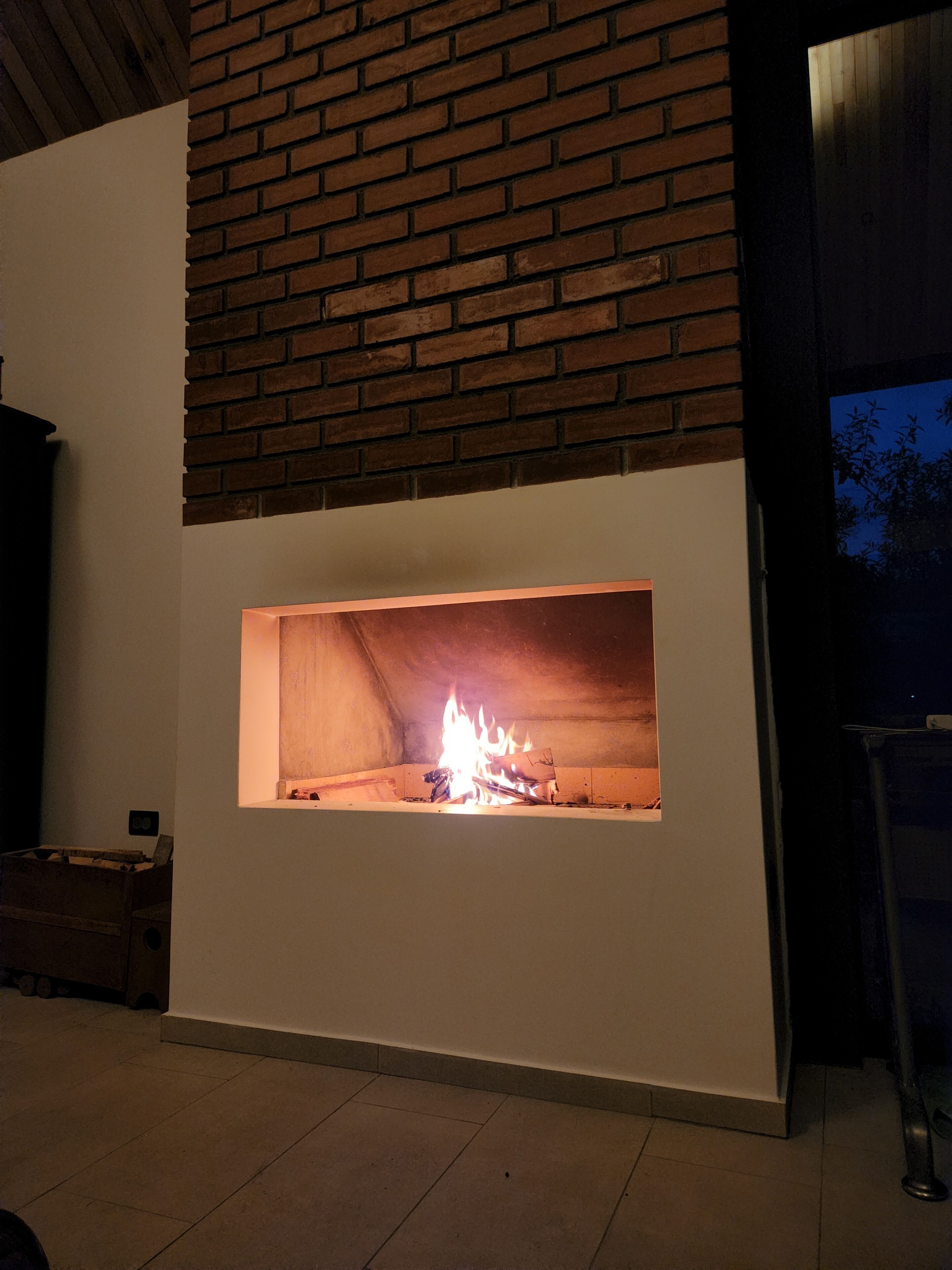 Een moderne haard met een bakstenen omlijsting, een witte muur en een betegelde vloer.
