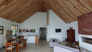 A spacious living area with a high wooden ceiling, a kitchen with modern appliances, and a fireplace.