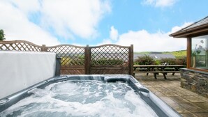A hot tub with a wooden fence and a picnic table in the background. - 5 Bed in Aberystwyth (oc-wan443) (Llanfarian)