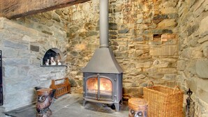 A stone-walled room with a wood-burning stove, a shelf with decorative items, and a woven basket. - 5 Bed in Aberystwyth (oc-wan443) (Llanfarian)