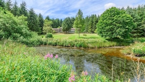 A serene landscape with a pond, lush greenery, and a house in the background. - 5 Bed in Snaizeholme (oc-w32200) (Hawes)