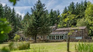 A stone house with a green roof and a conservatory, surrounded by dense forest and a grassy lawn. - 5 Bed in Snaizeholme (oc-w32200) (Hawes)