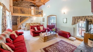 A spacious living area with a high wooden ceiling, a stone staircase, and a cozy red sofa set. - 5 Bed in Snaizeholme (oc-w32200) (Hawes)