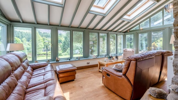 A sunroom with a large window, leather sofas, and a stone wall. - 5 Bed in Snaizeholme (oc-w32200) (Hawes)