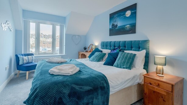 Ein Schlafzimmer mit einem großen Bett, einem Nachttisch, einem Sessel, einem Fenster mit Blick und einem Bild an der Wand.
