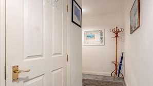 Ein Flur mit einer weißen Tür, einem gerahmten Bild an der Wand, einem Kleiderständer und einem blauen Regenschirm.