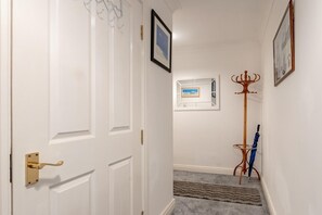 Ein Flur mit einer weißen Tür, einem gerahmten Bild an der Wand, einem Kleiderständer und einem blauen Regenschirm.