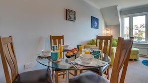 Ein Essbereich mit einem Glastisch, Holzstühlen und einer Schale mit Obst. Ein Fenster bietet Blick auf Gebäude.