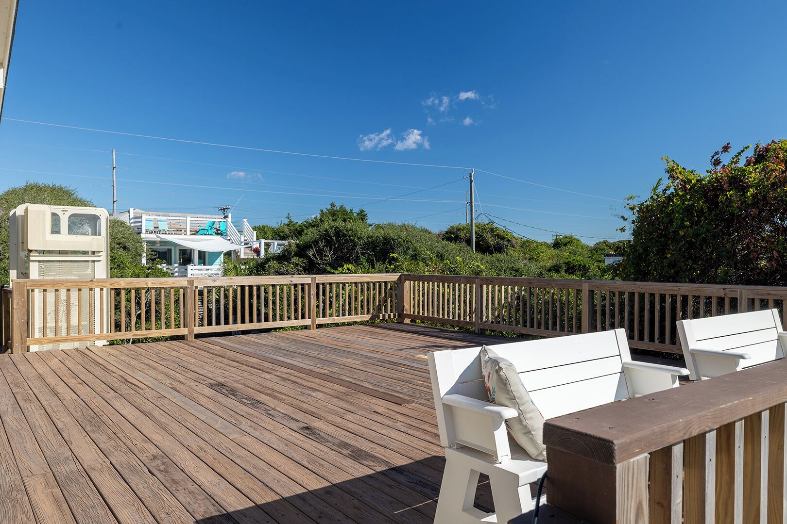 Une terrasse en bois avec des meubles d’extérieur blancs, un camping-car blanc et, au fond, un bâtiment doté d’un balcon.