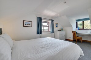 Ein Schlafzimmer mit einem großen Bett, einem Schreibtisch mit Stuhl, einem Heizkörper und einem Fenster mit Vorhängen.