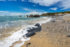 Une plage de galets et de rochers, avec des vagues et un ciel dégagé.