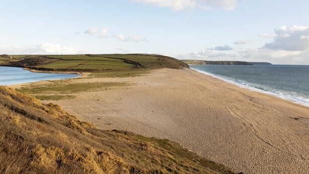 A coastal landscape with a pebbly beach, grassy hills, and cliffs in the distance. - 3 Bed in Gunwalloe (oc-p00858) (Gunwalloe)