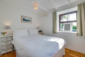 A bedroom with a bed, bedside tables, a lamp, a radio, a picture on the wall, and a window with curtains. - 3 Bed in Gunwalloe (oc-p00858) (Gunwalloe)