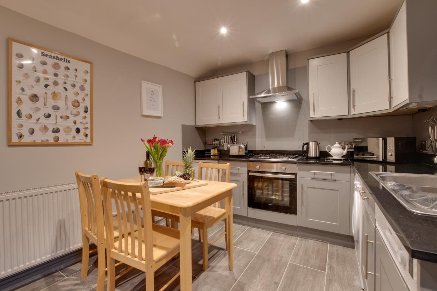 A modern kitchen with white cabinets, a stainless steel range hood, and a dining area with wooden chairs and a table.